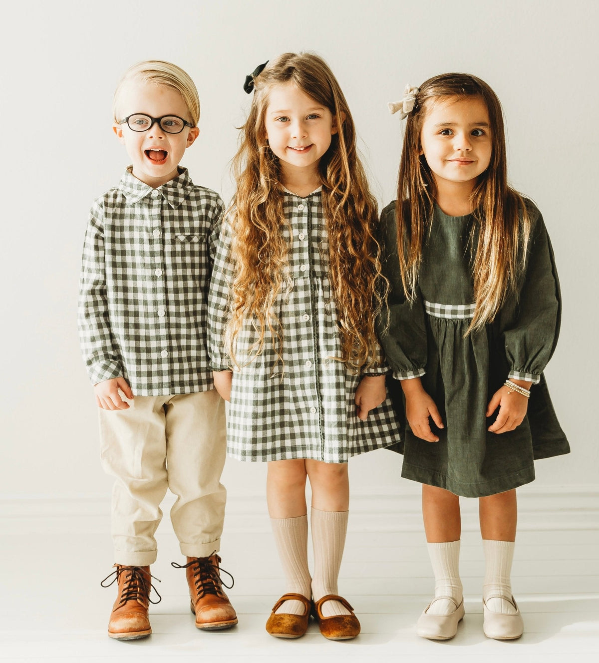 Three children wearing coordinating green outfits, including a boys’ green gingham shirt.