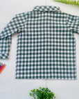 Back view of a green gingham long sleeve boys’ shirt beside colored pencils and greenery.