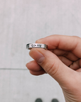 Hand holding the silver-tone Highs and Lows Ring to show its black faith symbols