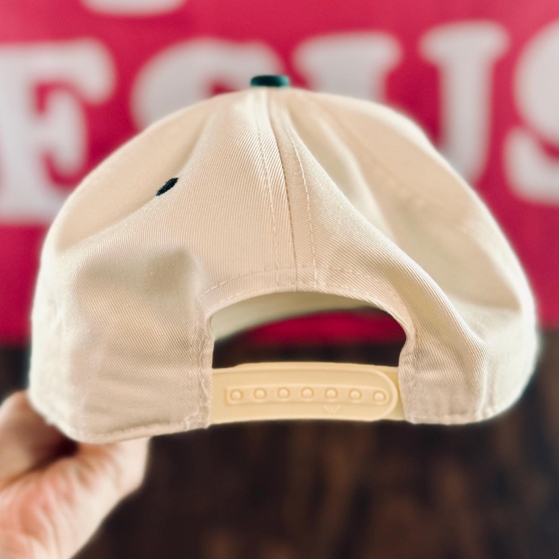 Beige cap held by a hand with a blurred background featuring text.