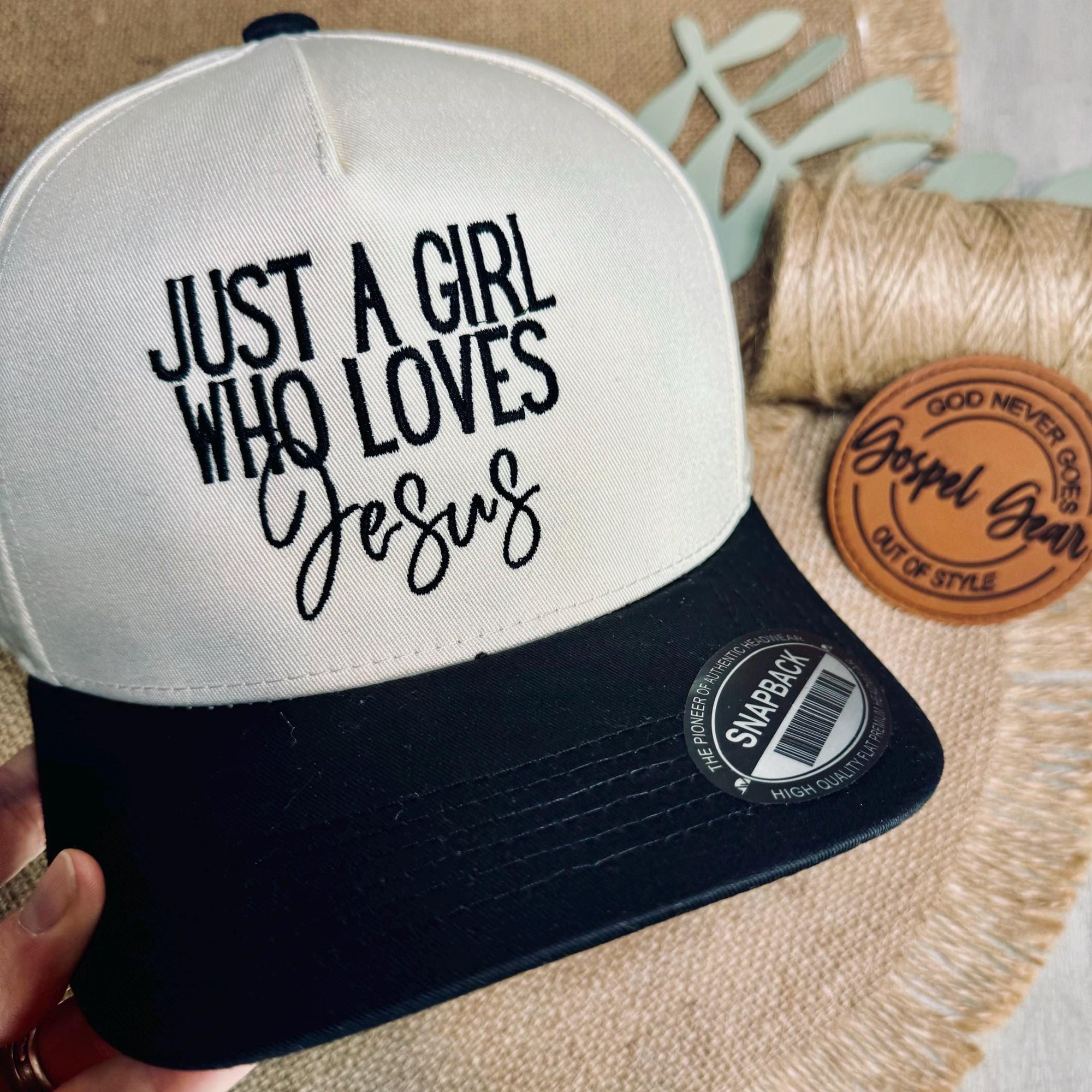 Cap with 'Just a Girl Who Loves Jesus' text held by a hand on a textured surface.