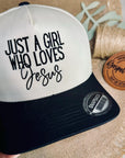 Cap with 'Just a Girl Who Loves Jesus' text held by a hand on a textured surface.