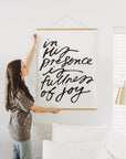 Woman displaying the 30 x 40 In His Presence wall art with wooden hanging rails beside a white sofa.