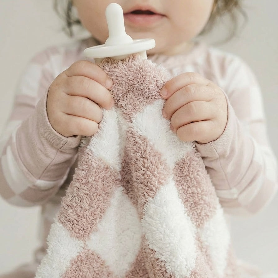 Child holding a textured pink and white blanket with a pacifier