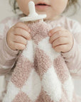 Child holding a textured pink and white blanket with a pacifier