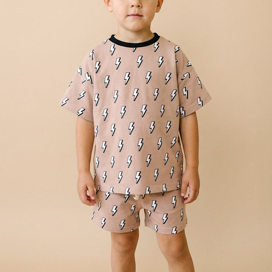 Child wearing a pink outfit with lightning bolt patterns on a beige background