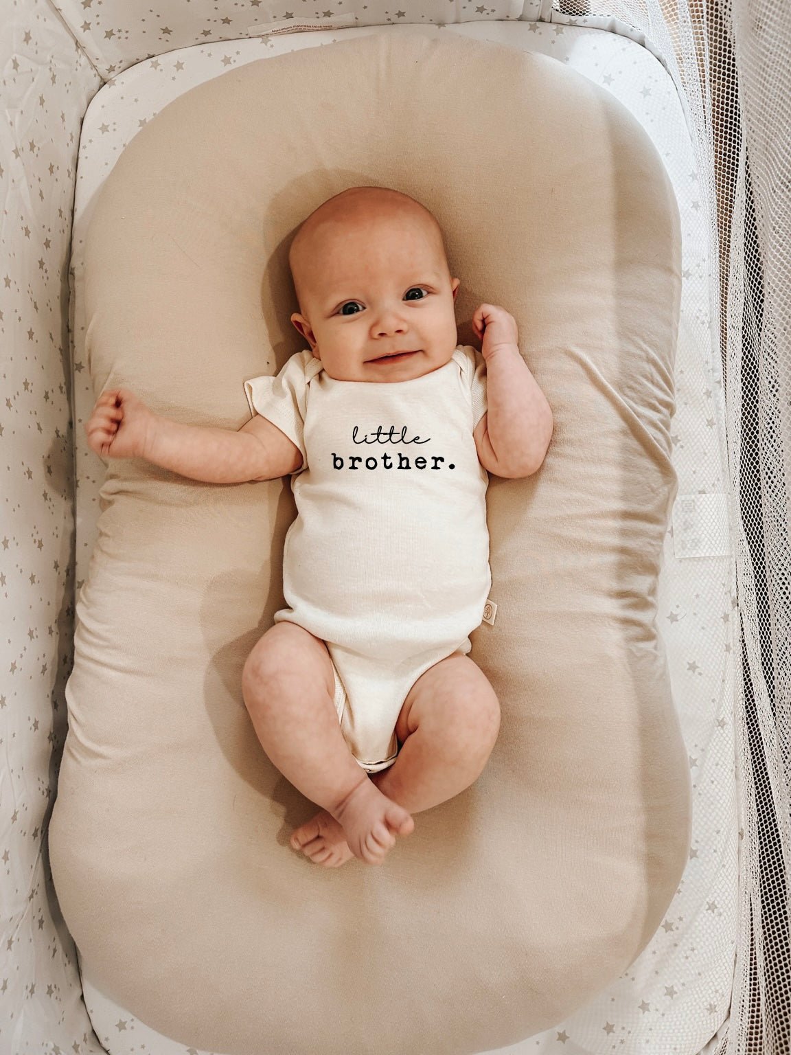 Baby lying in a cushioned lounger wearing a Little Brother organic cotton short sleeve bodysuit