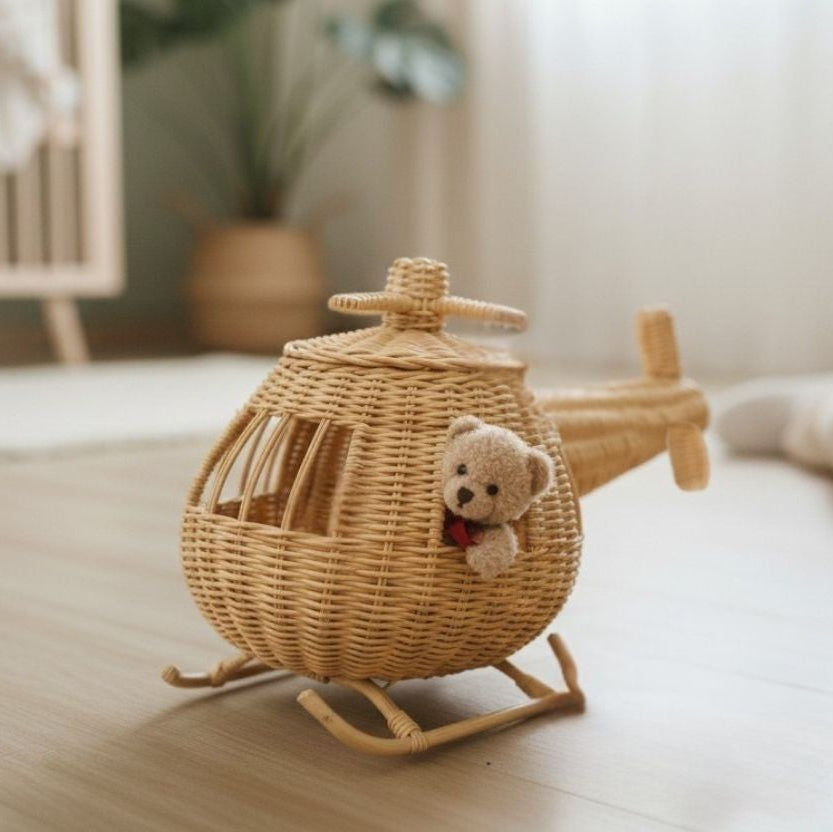 Wicker toy airplane with a teddy bear inside on a wooden floor.