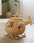 Wicker toy airplane with a teddy bear inside on a wooden floor.