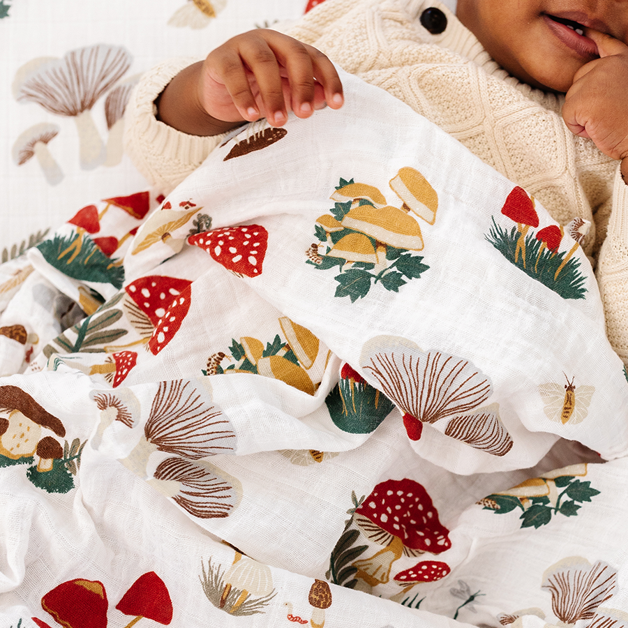 Baby wrapped in a blanket with a forest-themed pattern, surrounded by Christmas decorations.