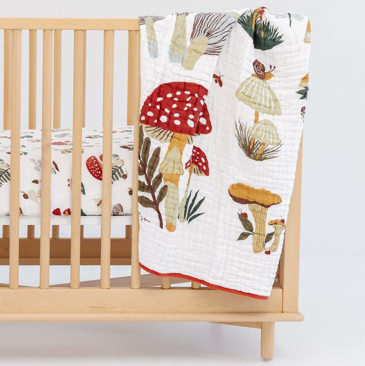Wooden crib with a colorful mushroom-patterned quilt draped over it on a white background