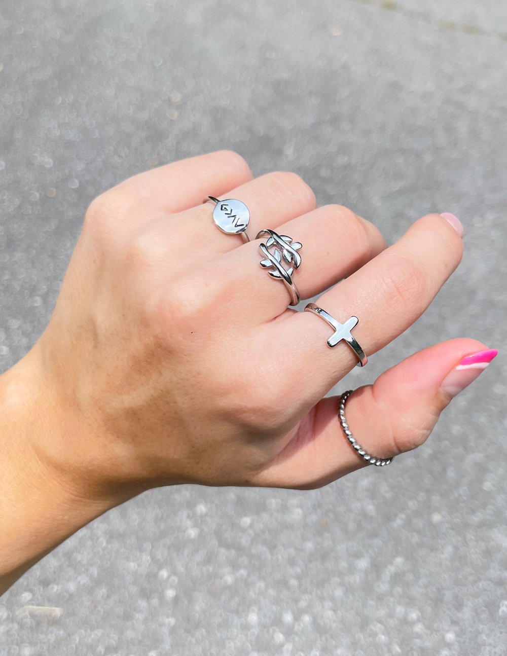 Silver-tone Olive Branch ring worn alongside other rings against a gray background
