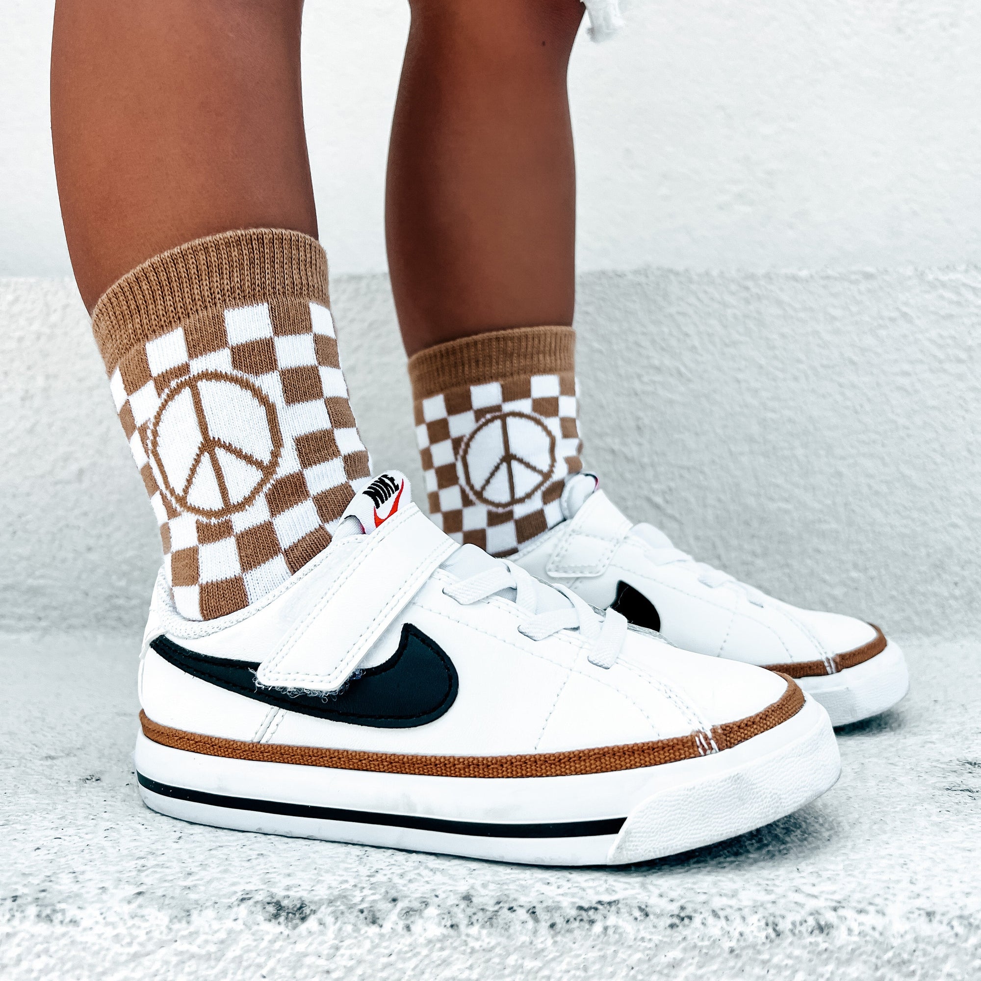 White sneakers with black accents worn with checkered socks featuring peace signs on a light gray background