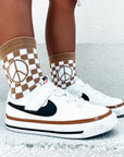 White sneakers with black accents worn with checkered socks featuring peace signs on a light gray background