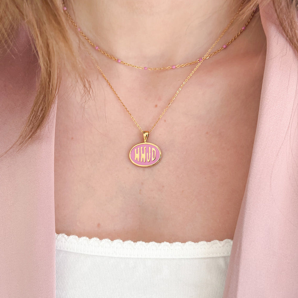 Necklace with a pink pendant featuring initials on a person wearing a light pink top.