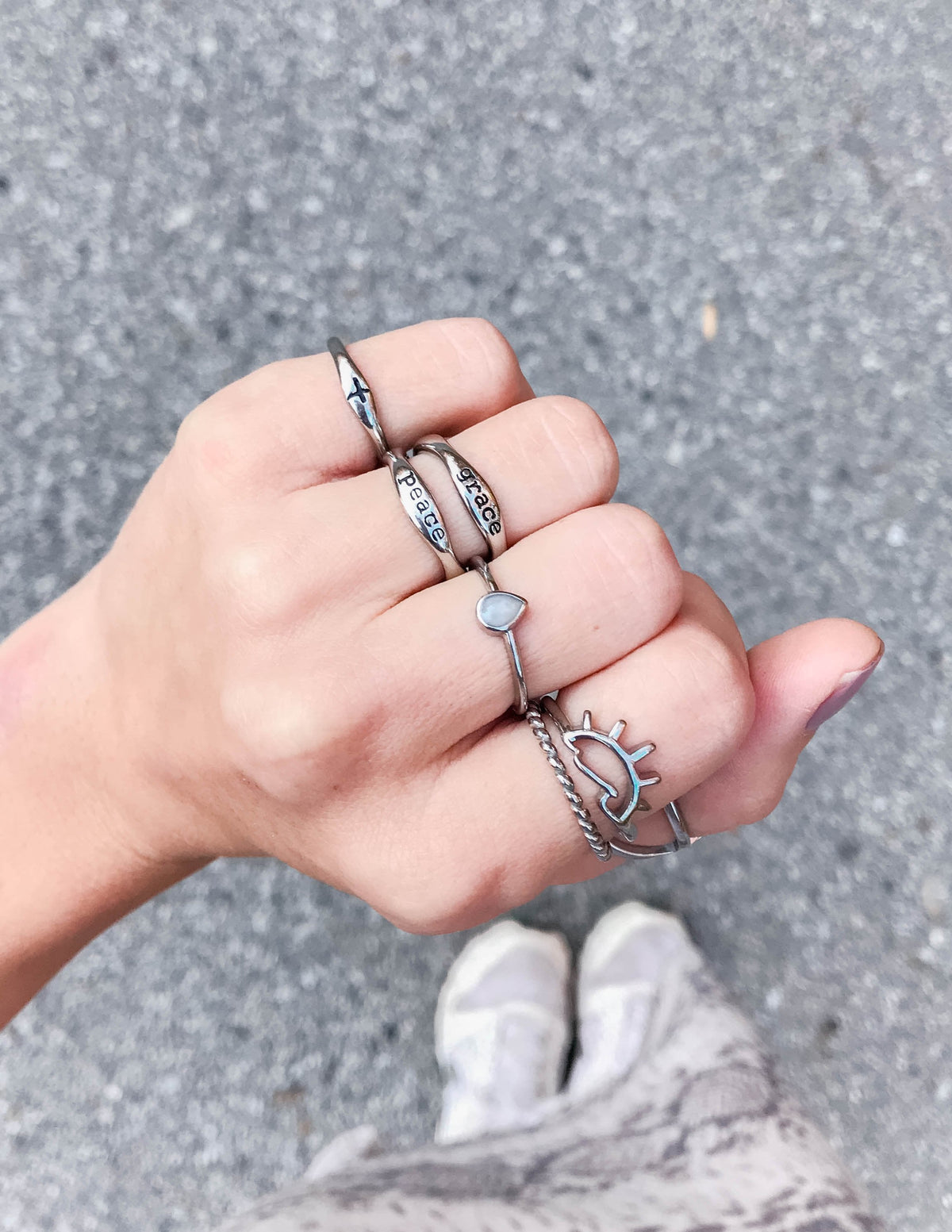 Silver-tone cross promise ring styled with other rings on a hand outdoors