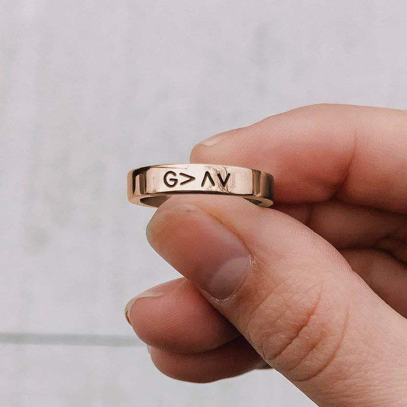 Rose gold ring with engraved symbols held by a hand against a light background
