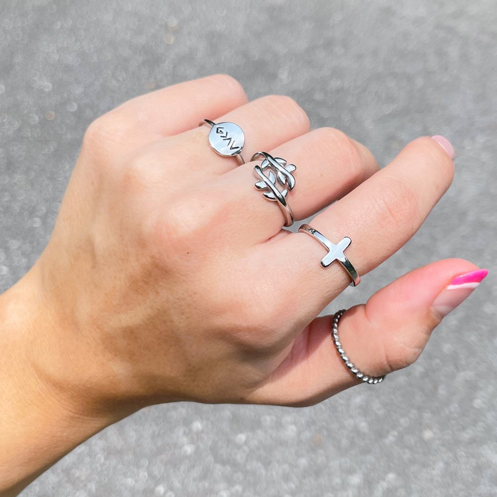 Hand wearing multiple silver rings on a gray pavement background
