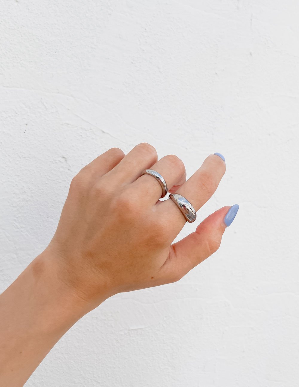Hand wearing two silver rings on a light gray background