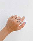 Hand wearing two silver rings on a light gray background