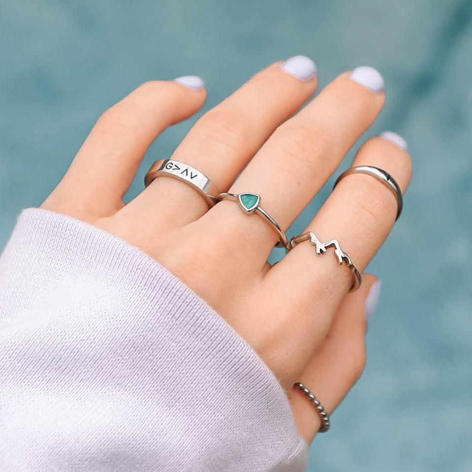 Hand wearing multiple silver rings with a blurred teal background