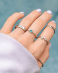 Hand wearing multiple silver rings with a blurred teal background